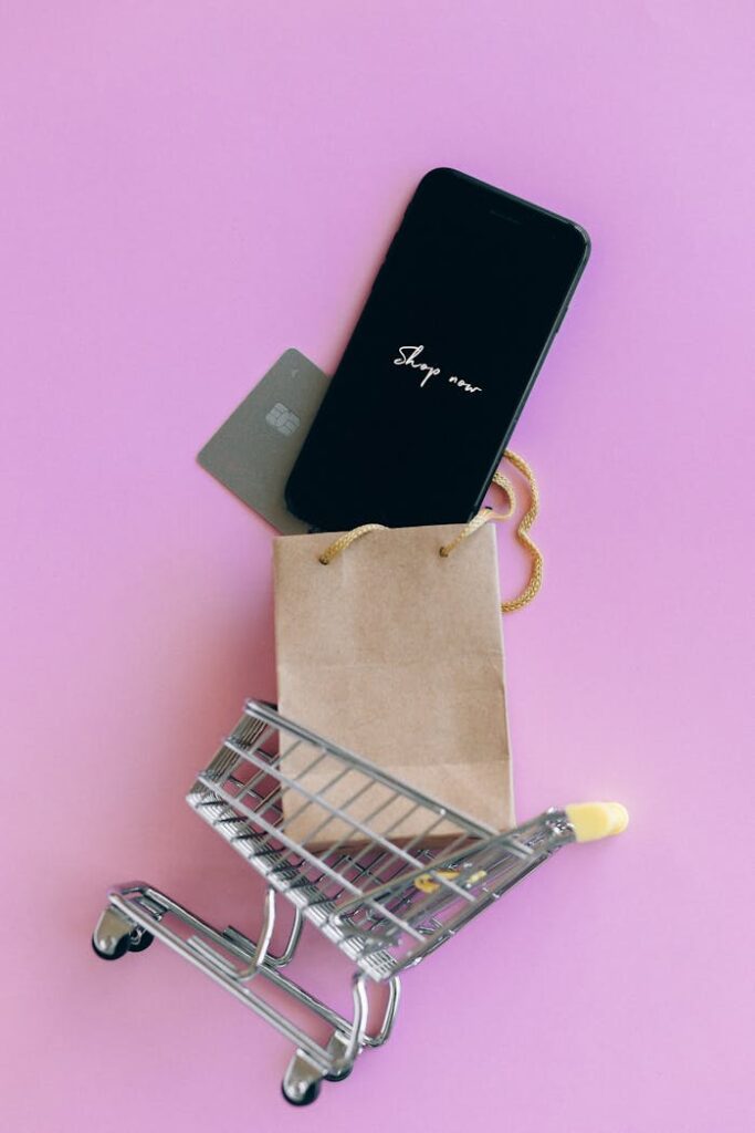 pexels-photo-6214450 A smartphone, credit card, and bag in a miniature shopping cart on a pink background.